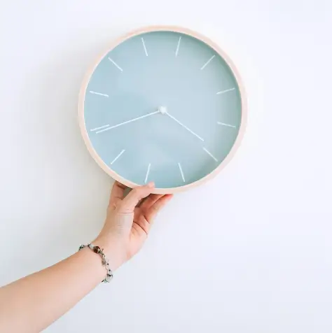 Hand holding a clock in front of a blue wallpaper